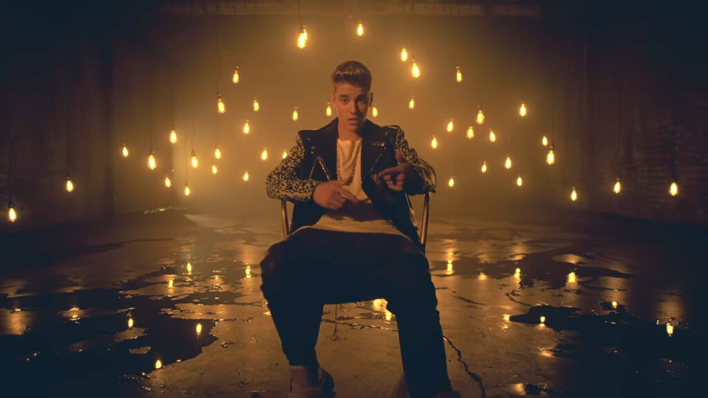 Justin Bieber is sitting on a chair in a dimply lit room