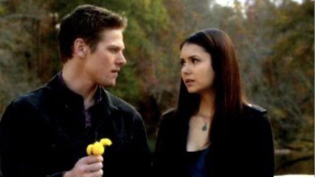 Matt and Elena having a conversation outdoors, with Matt holding a small yellow flower in a scene from The Vampire Diaries.
