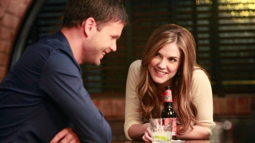 Alaric and Jenna sitting together at what appears to be a restaurant or bar, both smiling and enjoying each other's company.
