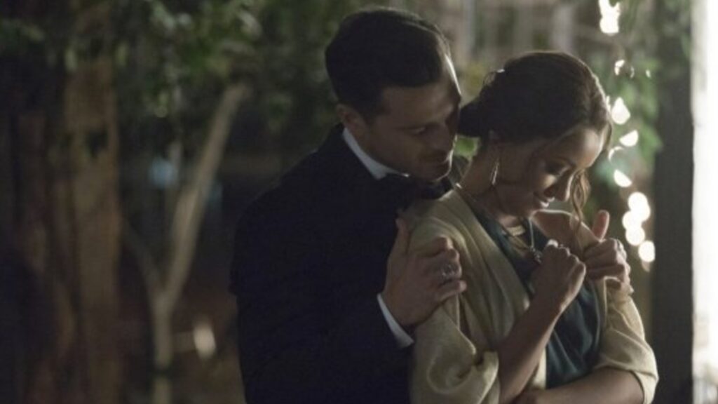 Bonnie and Enzo in formal clothing embracing outdoors at night with atmospheric lighting.