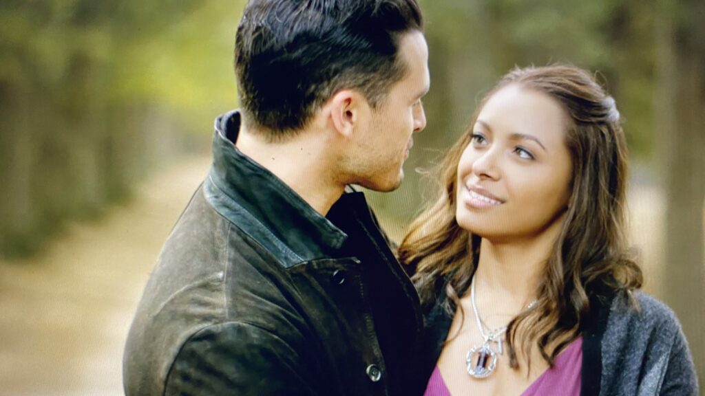 Bonnie and Enzo in an intimate outdoor moment during daytime, with Enzo wearing a leather jacket and Bonnie smiling warmly at him.