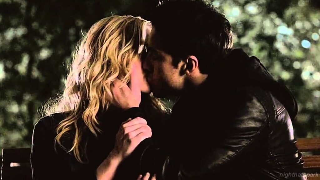 Caroline and Tyler sharing an intimate moment outdoors at night, with Caroline's blonde hair and Tyler in dark clothing.