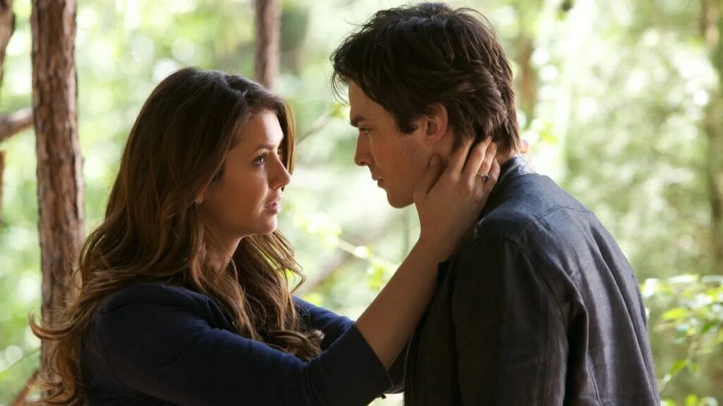 Elena and Damon in a romantic forest scene, with Elena touching Damon's face as they gaze at each other.