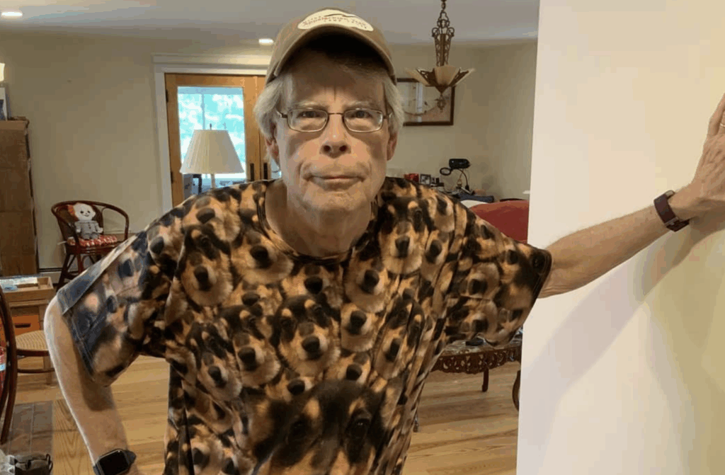 Stephen King, wearing a brown cap, and a T-shirt, filled with pictures of his dog.