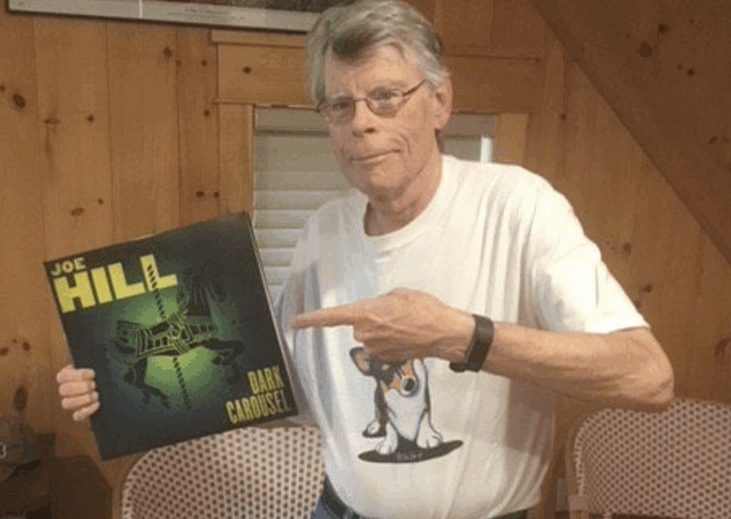 Stephen King posing with a viny record, wearing a white shirt.