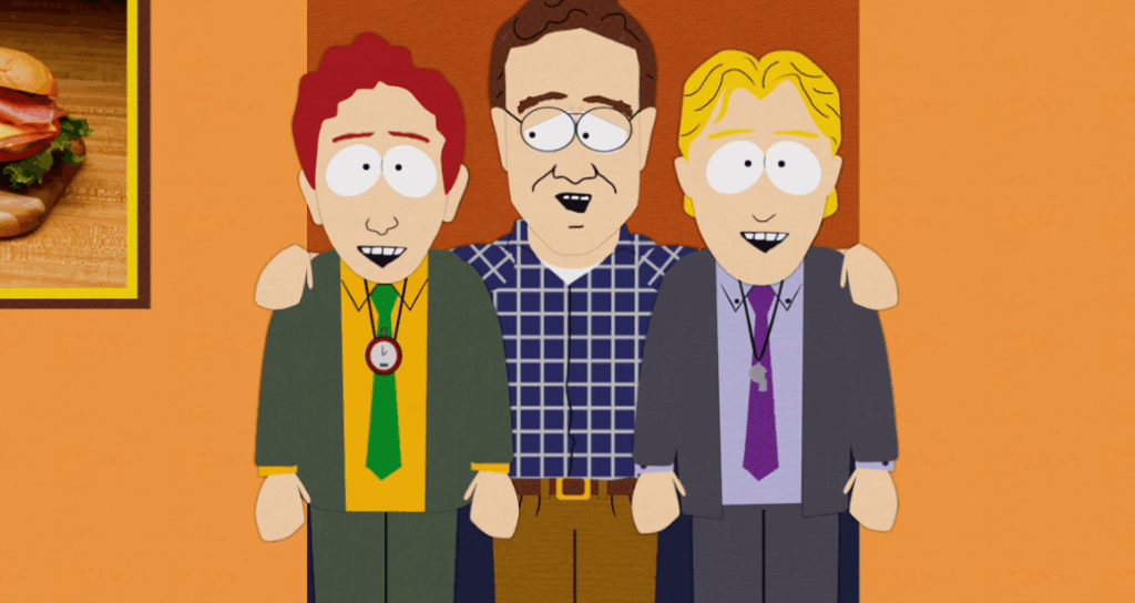 Three men are standing together and smiling. The man in the middle, wearing glasses and a plaid shirt, has his arms around the shoulders of the two men next to him.
