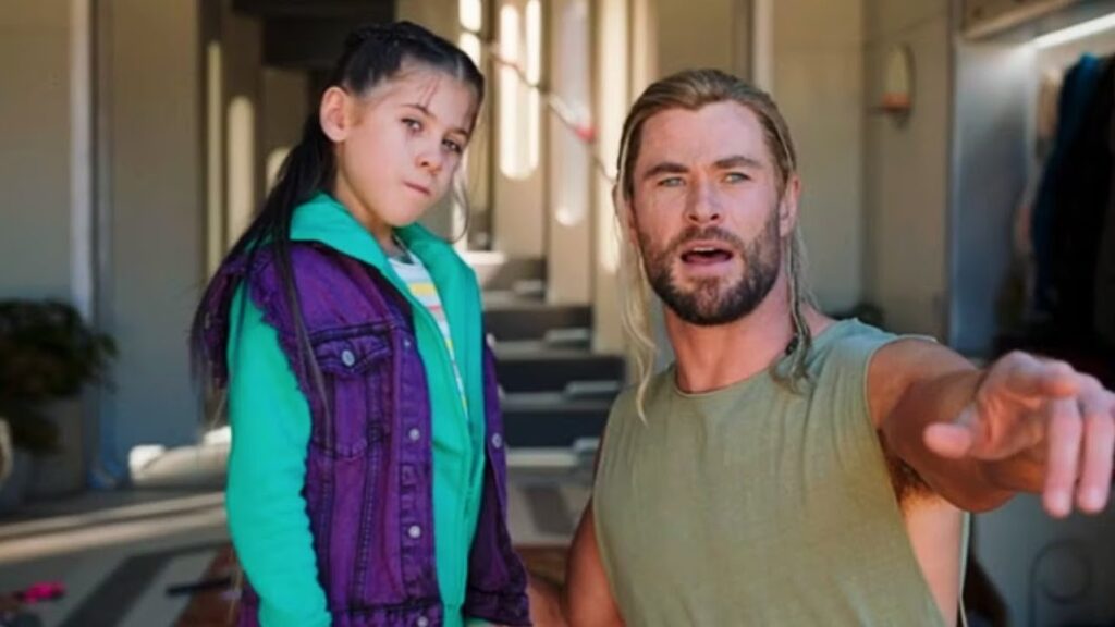 Thor in casual modern clothes standing next to Love, a young girl wearing a teal hoodie and purple jacket, both looking serious as Thor points off-screen.
