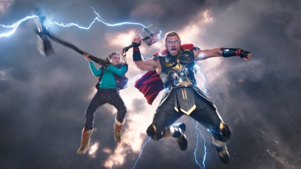 An action scene showing Love wielding Stormbreaker while Thor flies through the air in his armor, both surrounded by lightning and dramatic storm clouds.