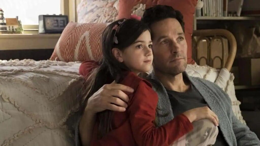 Scott Lang and his daughter Cassie Lang sitting together in a cozy living room setting, with Cassie wearing a red cardigan and Scott in casual clothes, both looking contemplative.