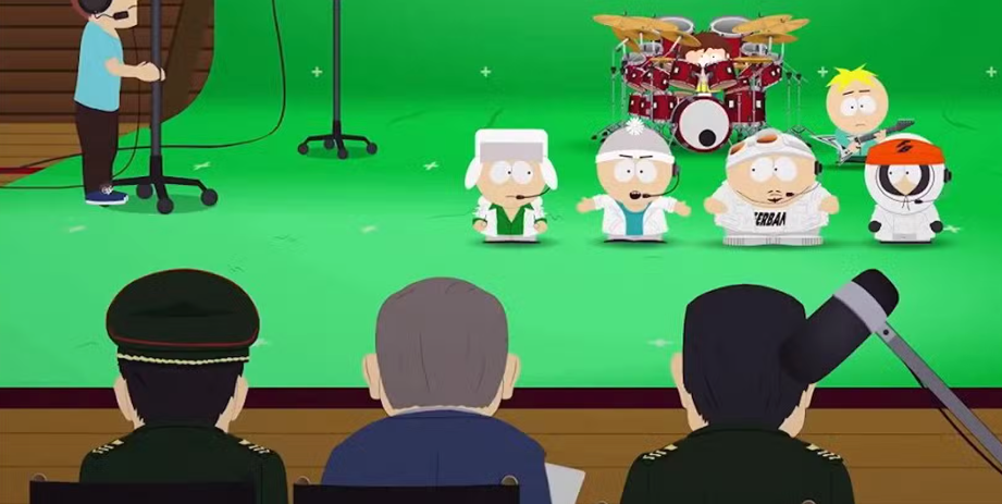 Four boys from the show, including Cartman and Kenny, on a green screen set, dressed in white tracksuits and holding microphones. Three men in military attire are sitting in the foreground, watching the boys perform.