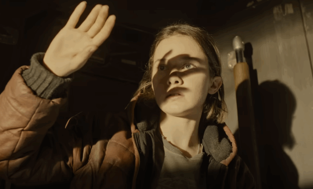 A girl with short hair, wearing a brown jacket, and holding up her hand to block the bright light in Alien: Romulus.