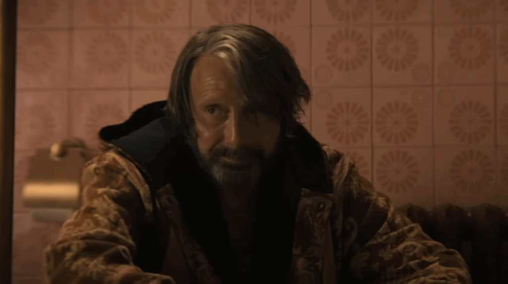 Mads Mikkelsen with a full beard, medium-length hair, and a jacket in Dust Bunny. 