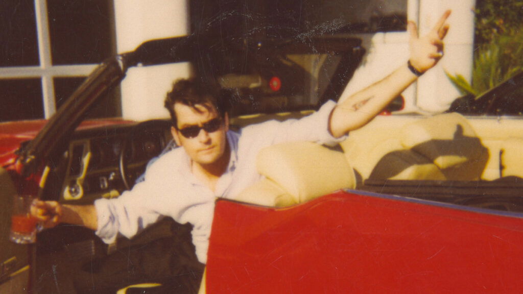 Charlie Sheen posing from inside a red car