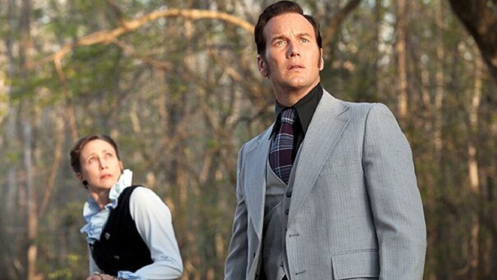 Patrick Wilson as Ed Warren and Vera Farmiga as Lorraine Warren in The Conjuring: The Devil Made Me Do It, both wearing more modern 1980s attire while investigating outdoors