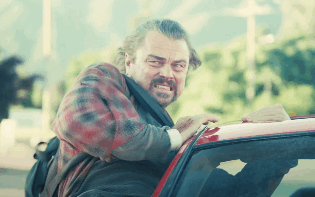 Leonardo Dicaprio, preparing to jump out of a car in One Battle After Another.