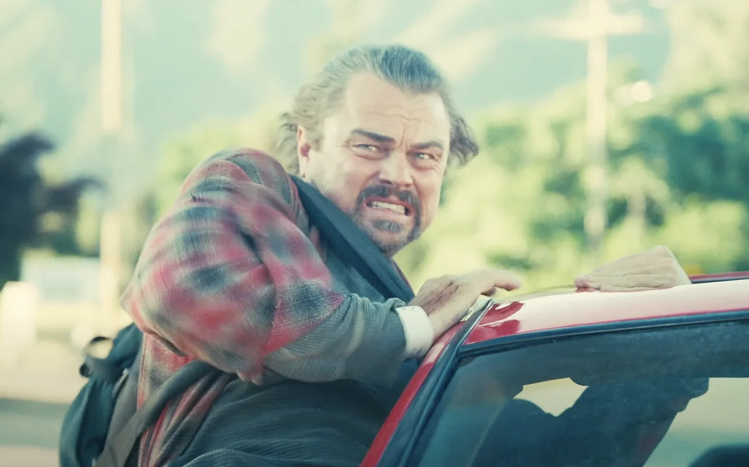 Leonardo Dicaprio, preparing to jump out of a car in One Battle After Another.