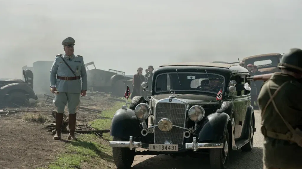 A man walking beside a car in a still from Nuremberg