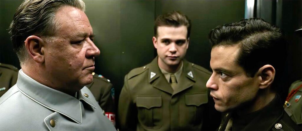 Russell Crowe and Rami Malek standing face-to-face with a soldier in the backdrop in Nuremberg