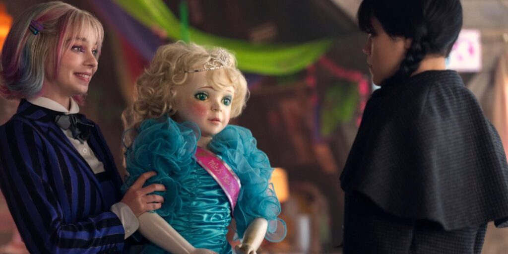 Enid Sinclair smiling and holding a doll as Wednesday Addams stands in front of her in Wednesday season 2
