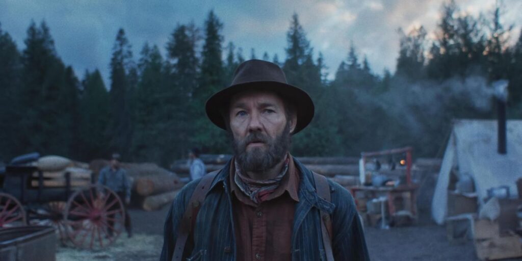 Joel Edgerton in Train Dreams wearing a hat and looking alert