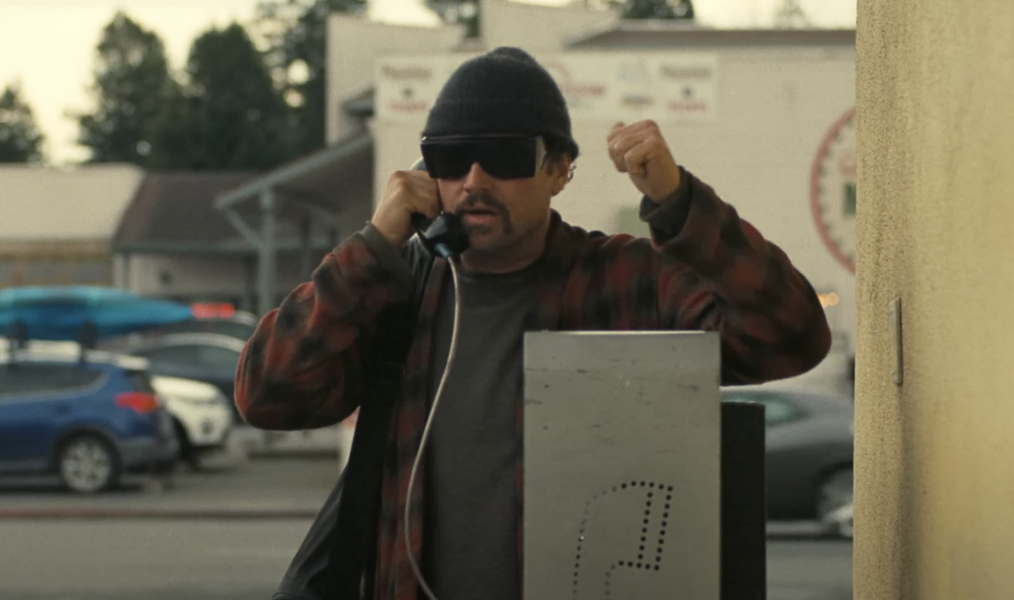 Leonardo DiCaprio using a phone booth in One Battle After Another. 