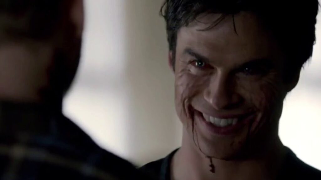 Ian Somerhalder as Damon Salvatore with dark hair smiling menacingly with blood visible on his mouth and chin, photographed in close-up with dramatic lighting.