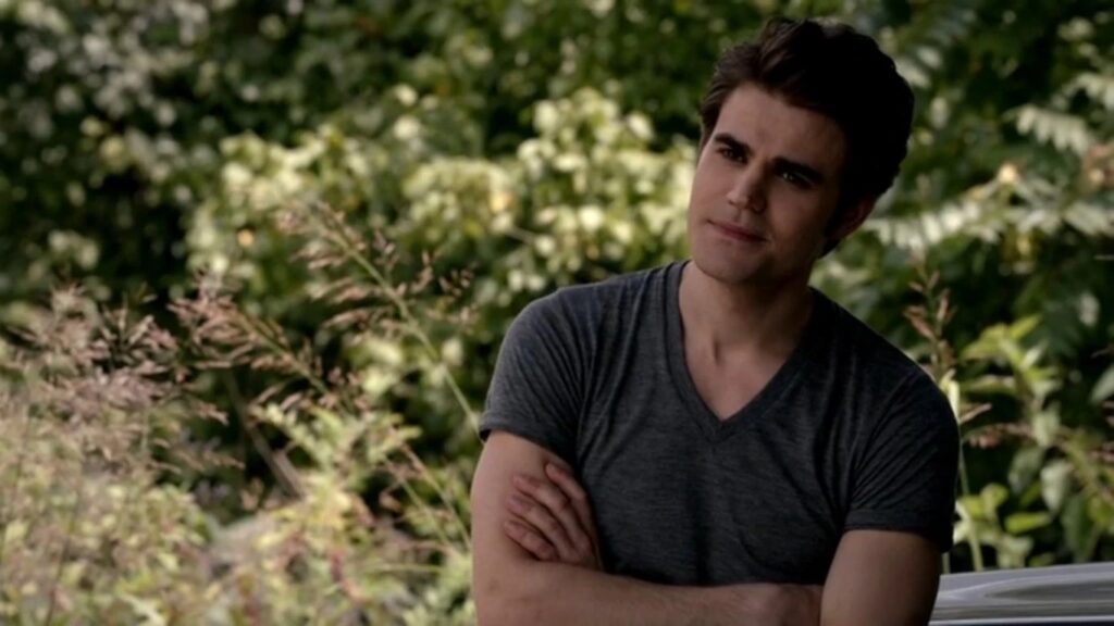 Paul Wesley as Silas with dark hair wearing a gray v-neck shirt, sitting outdoors with his arms crossed and a contemplative expression.