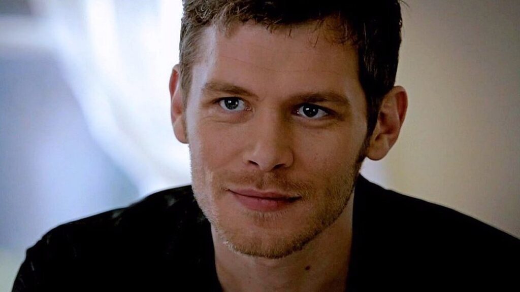 Joseph Morgan as Klaus Mikaelson with short dark hair and light eyes wearing a dark henley shirt, smiling slightly at the camera.