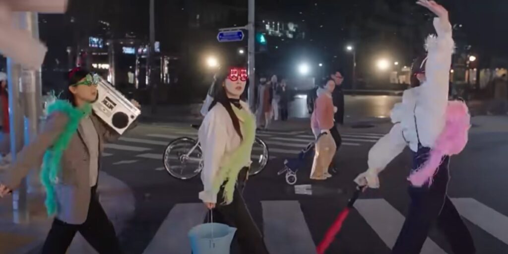 3 characters walking on a zebra crossing dressed up in colorful and bright clothing at night in the To The Moon s how. It's meant to mirror the Beatles' walk. 
