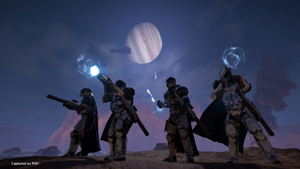 Helldivers 2 screenshot shows four players standing in formation to defend against an approaching Terminid horde.