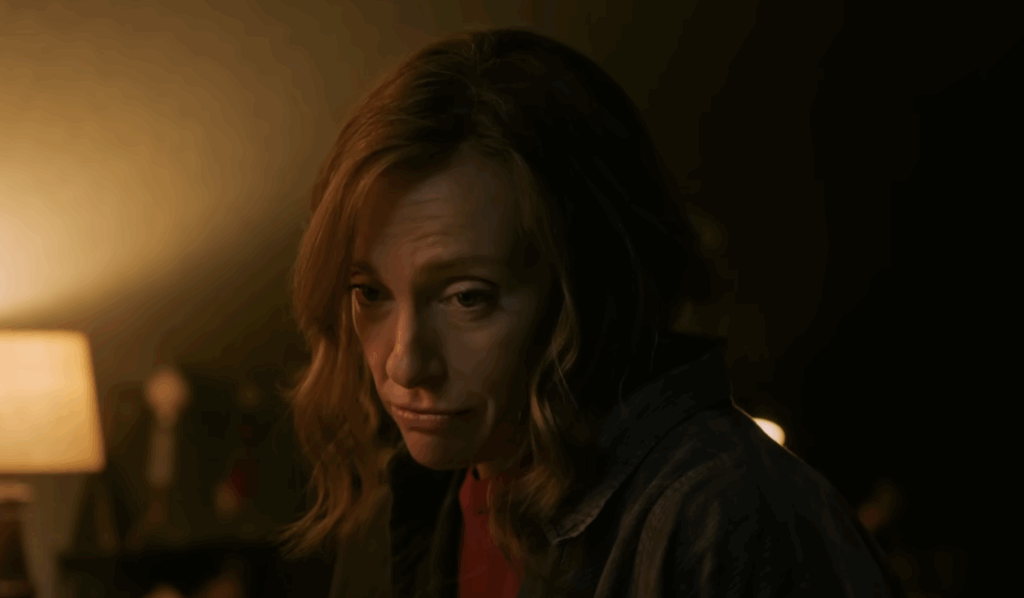 A woman with blonde hair, sitting alone in a lamp's light.