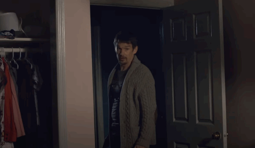 Ethan Hawke, wearing a sweater and standing in a doorway.