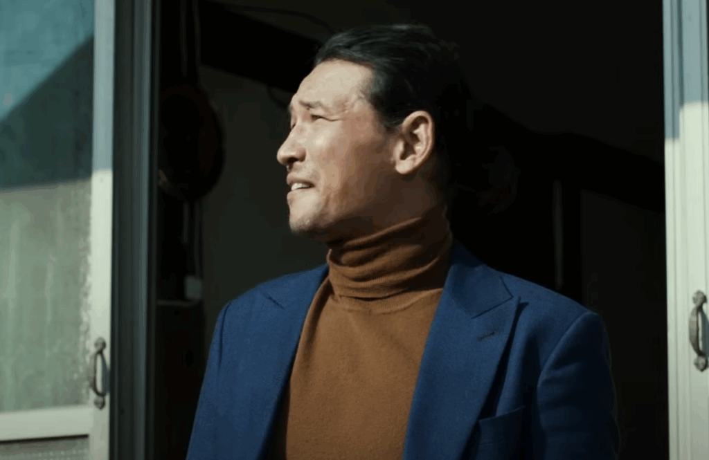 A man in a brown turtle-neck shirt, and a dark blue blazer in The Wailing.