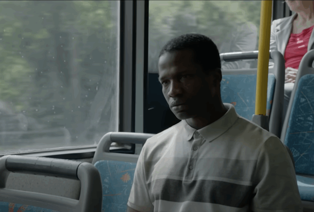 A man, wearing a striped polo T-shirt, sitting alone in a bus.