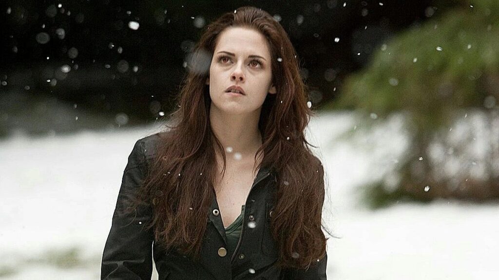 Bella (Kristen Stewart) after her vampire transformation stands in falling snow wearing a dark jacket, capturing the atmospheric and moody tone.