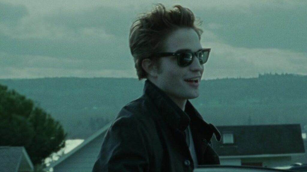 Edward (Robert Pattinson) wearing sunglasses with a slight smile, showing a rare moment of his more relaxed and playful side in a still from the first Twilight film.