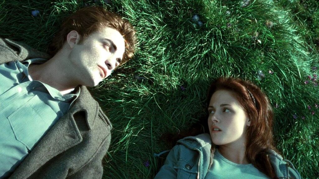 Edward (Robert Pattinson) and Bella (Kristen Stewart) lie together peacefully on green grass during the first film. Edward's skin is shining like diamonds as the sun-rays hit his face.