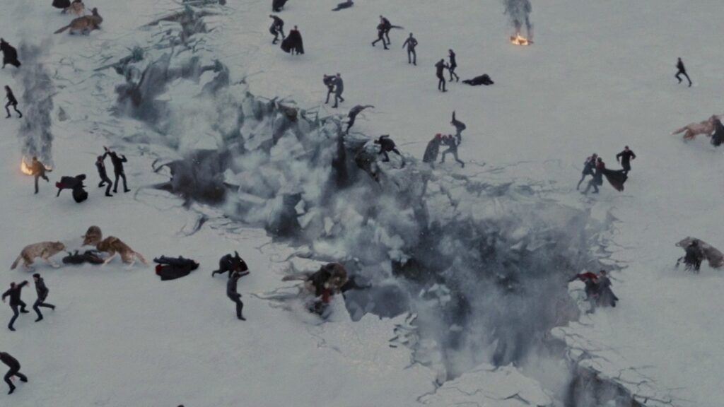 An aerial view of the chaotic battle scene involving vampires and werewolves in Breaking Dawn Part 2, with smoke, fighting figures, and casualties scattered across the snowy battlefield.