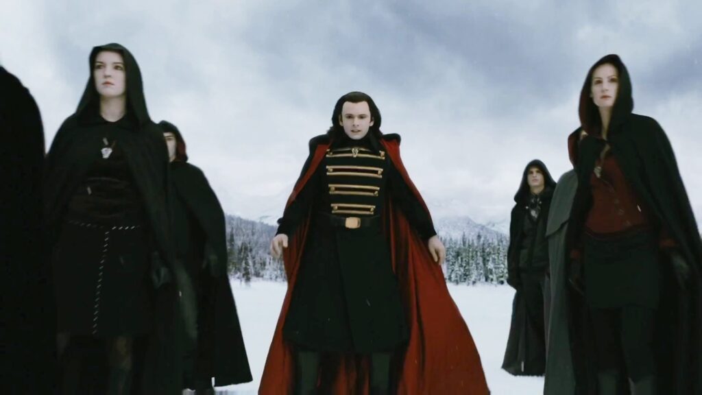The Volturi vampires, led by Aro (played by Michael Sheen) in his distinctive red and black cloak with gold detailing, stand imposingly in the snow during the climactic scene from Breaking Dawn Part 2.