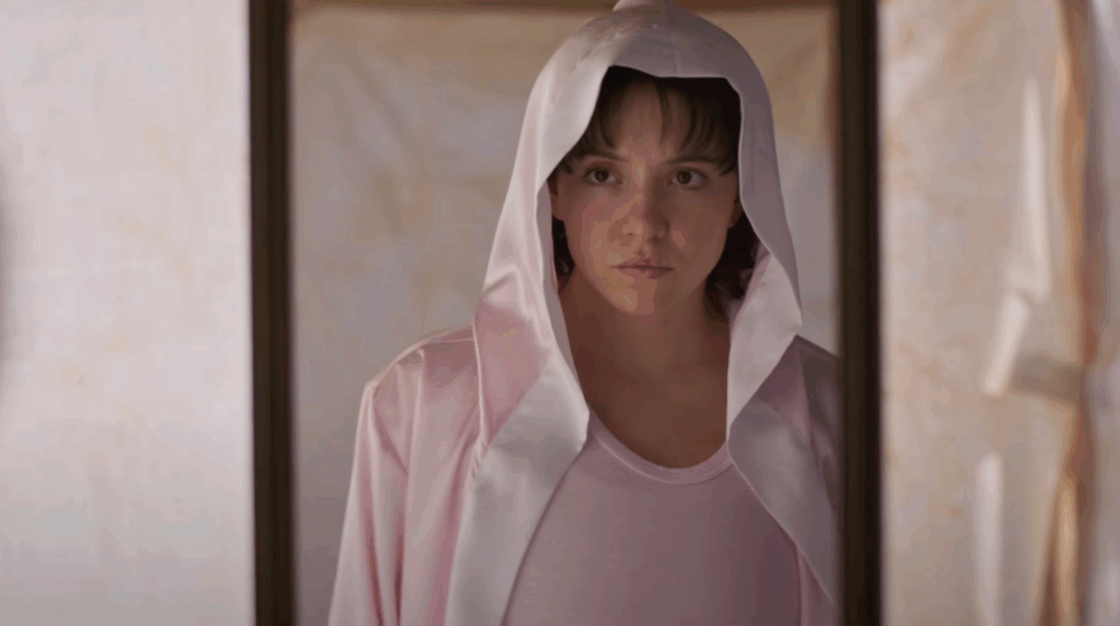 Sydney Sweeney in a hoodie looking at a mirror