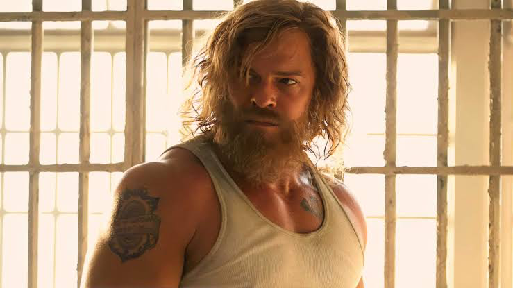 Alan Ritchson in unkempt hair behind prison bars in Motor City.