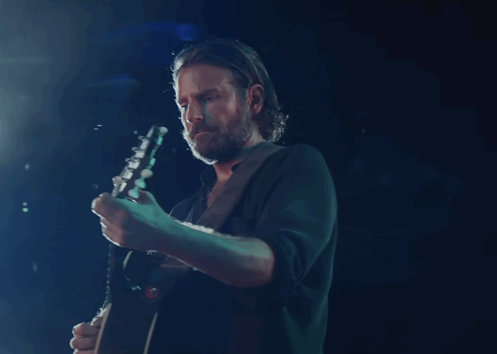 Bradley Cooper performing and holding a guitar. 