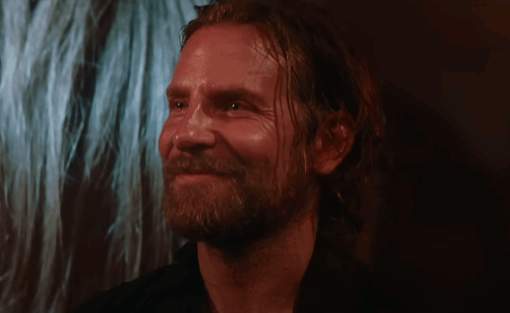 Bradley Cooper, smiling at Lady Gaga's performance. 