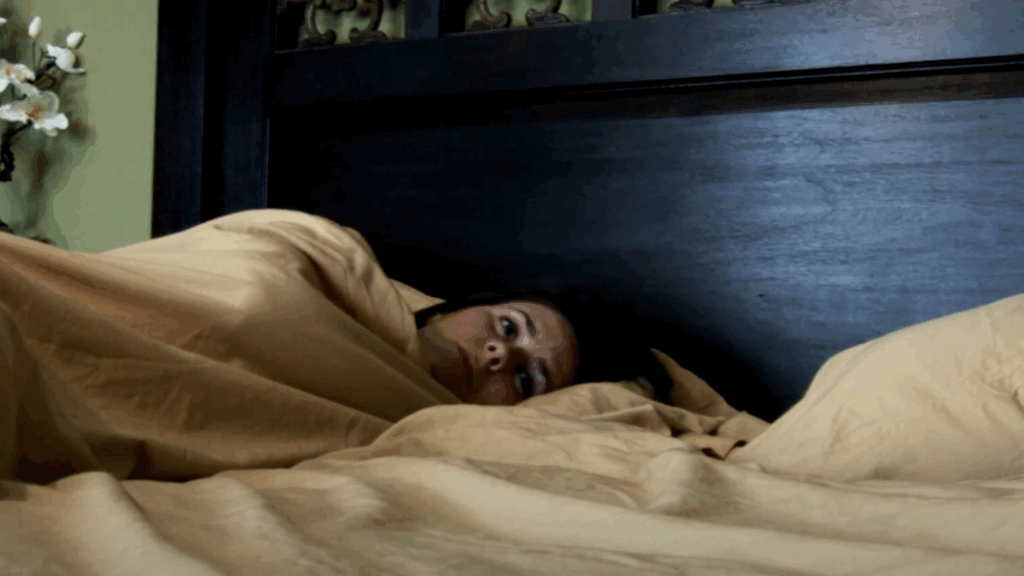 A woman lying down on a bed with her eyes open in Paranormal Activity.