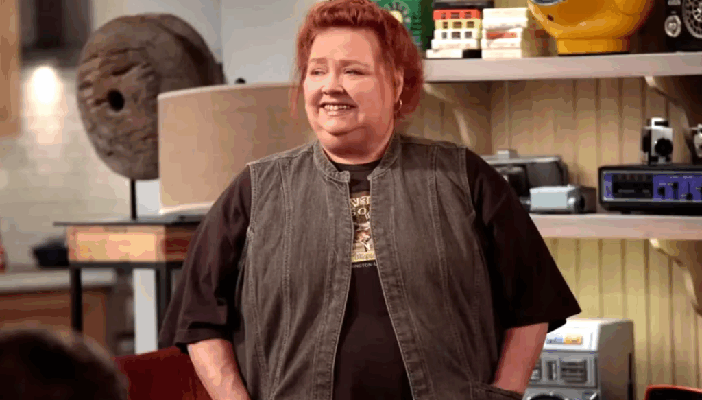 Berta is smiling, standing with her hands in the pockets of her vest.