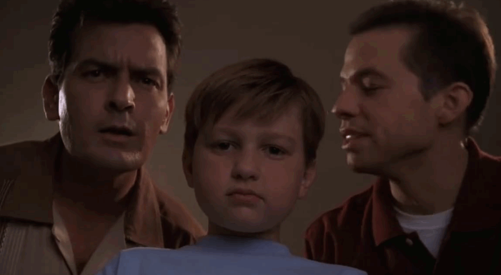 Jake with a serious face is standing between the Charlie and Alan.