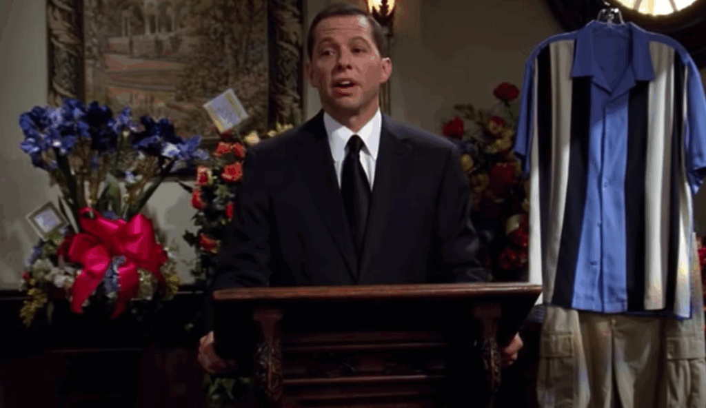 Alan Harper is dressed in a suit and standing at a podium, with a rack of clothing right next to him.