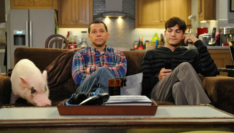 Alan Harper is sitting on a couch with his arms crossed, next to Walden Schmidt and a pig.