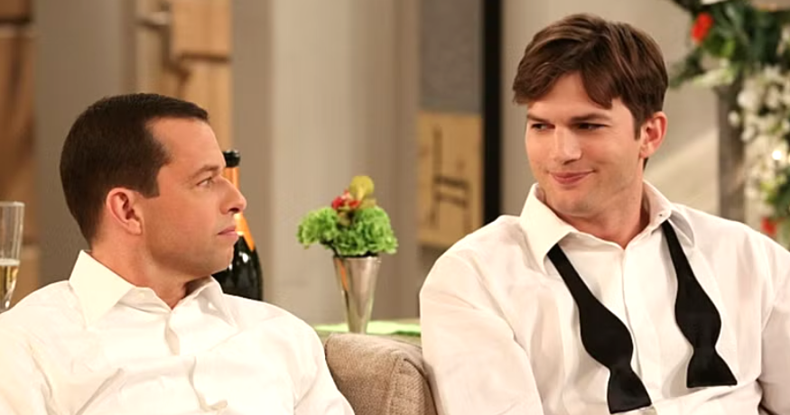 Walden Schmidt is sitting on a couch with Alan Harper, wearing a tuxedo shirt with his bowtie untied and looking at Alan with a smirk.