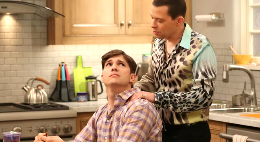 Walden Schmidt is sitting at a kitchen counter, looking upwards as Alan Harper puts a hand on his shoulder.